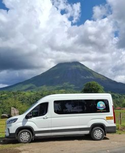 White JTC Transfer van offering Private Costa Rica airport transportation service. Parked with Arenal Volcano in the background