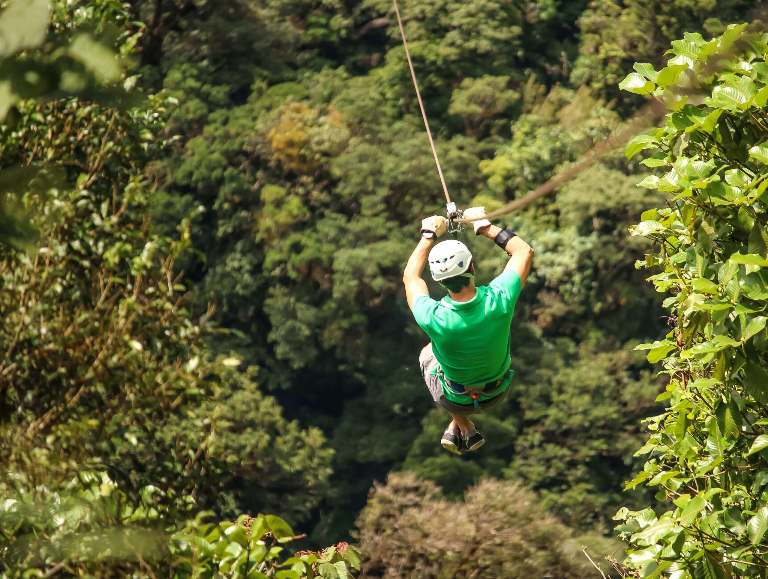 http://Adventurer%20in%20a%20green%20shirt%20and%20helmet%20ziplining%20above%20the%20dense%20Costa%20Rica%20rainforest%20canopy