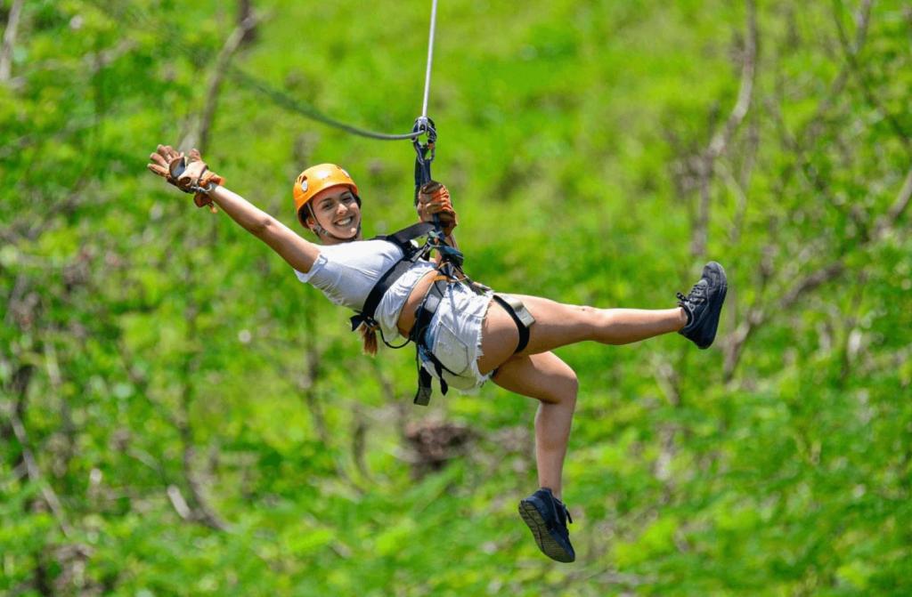 Smiling woman wearing helmet and harness ziplining above dense Costa Rica rainforest canopy during a canopy/zipline adventure near Jaco beach
